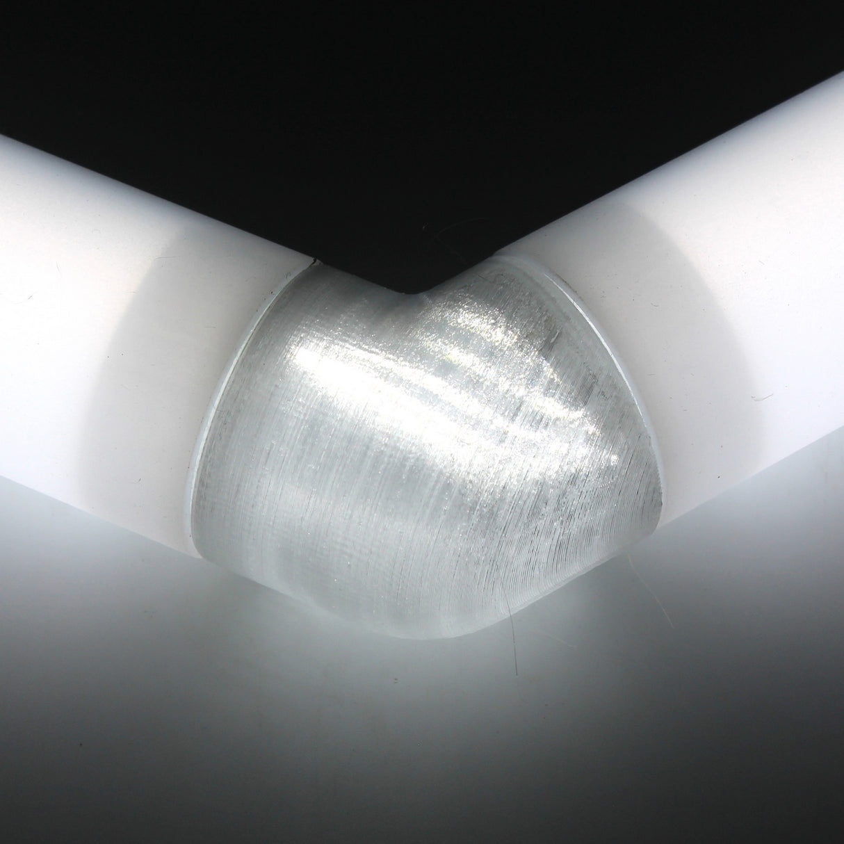 Close-up of a white Oslo diffuser tube forming a corner, connected by a Translucent Elbow for Oslo Profile beneath a black surface.