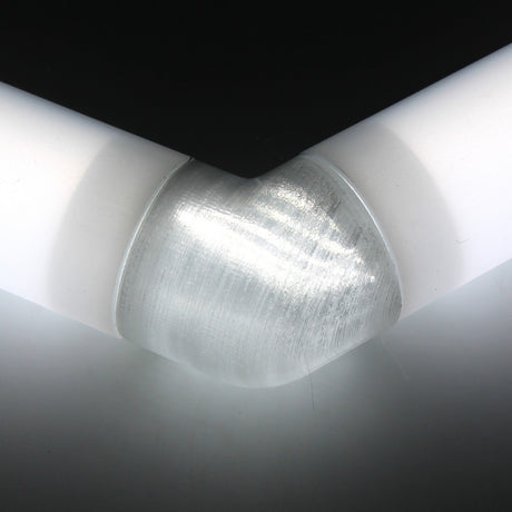 Close-up of a white Oslo diffuser tube forming a corner, connected by a Translucent Elbow for Oslo Profile beneath a black surface.