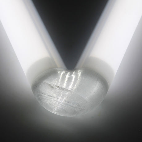 A close-up of the rounded end of a Translucent Elbow for Oslo Profile placed between two parallel white light tubes, forming a V-shaped pattern of light and shadow on a neutral background.