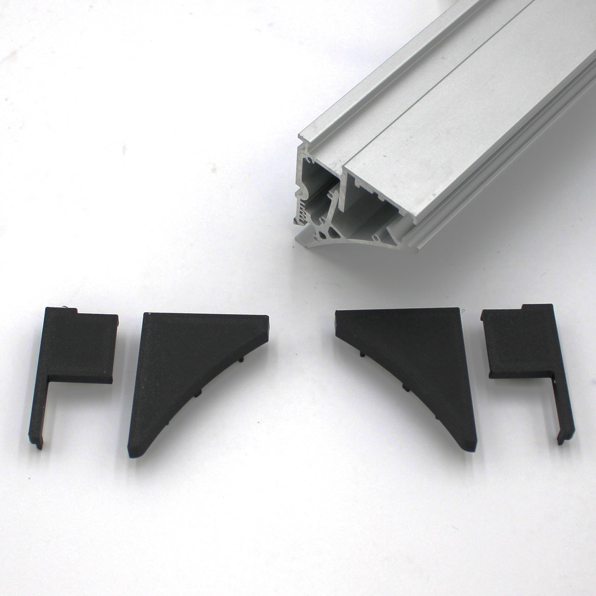 Shown on a white surface is a silver aluminum Pula P10 edge-lit shelf profile above four black plastic End Cap for Pula P10 Profile connectors.