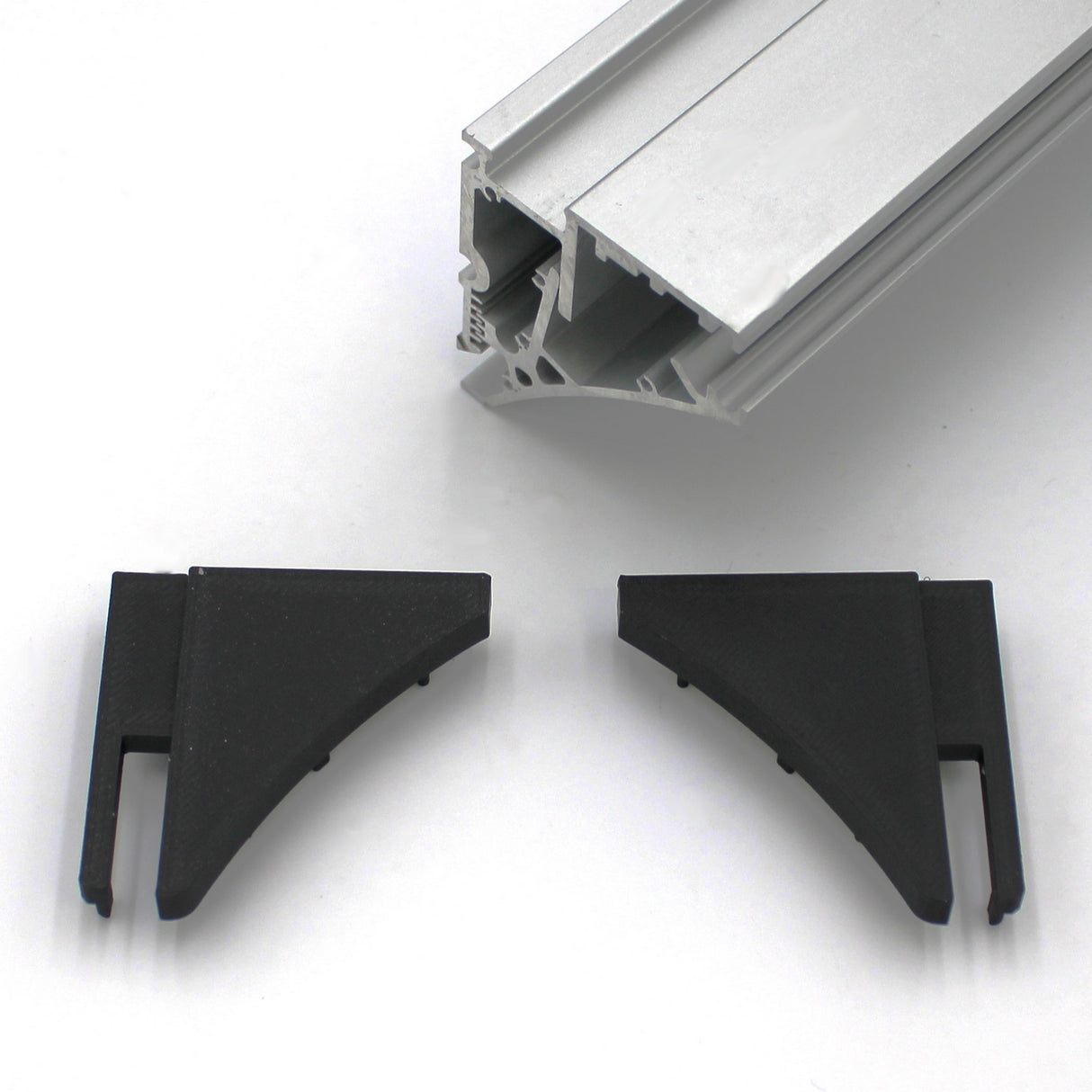 A close-up of the End Cap for Pula P10 Profile with two black plastic corner connectors and an aluminum extrusion, all on a white surface—ideal for finishing the Pula P10 edge-lit shelf profile.