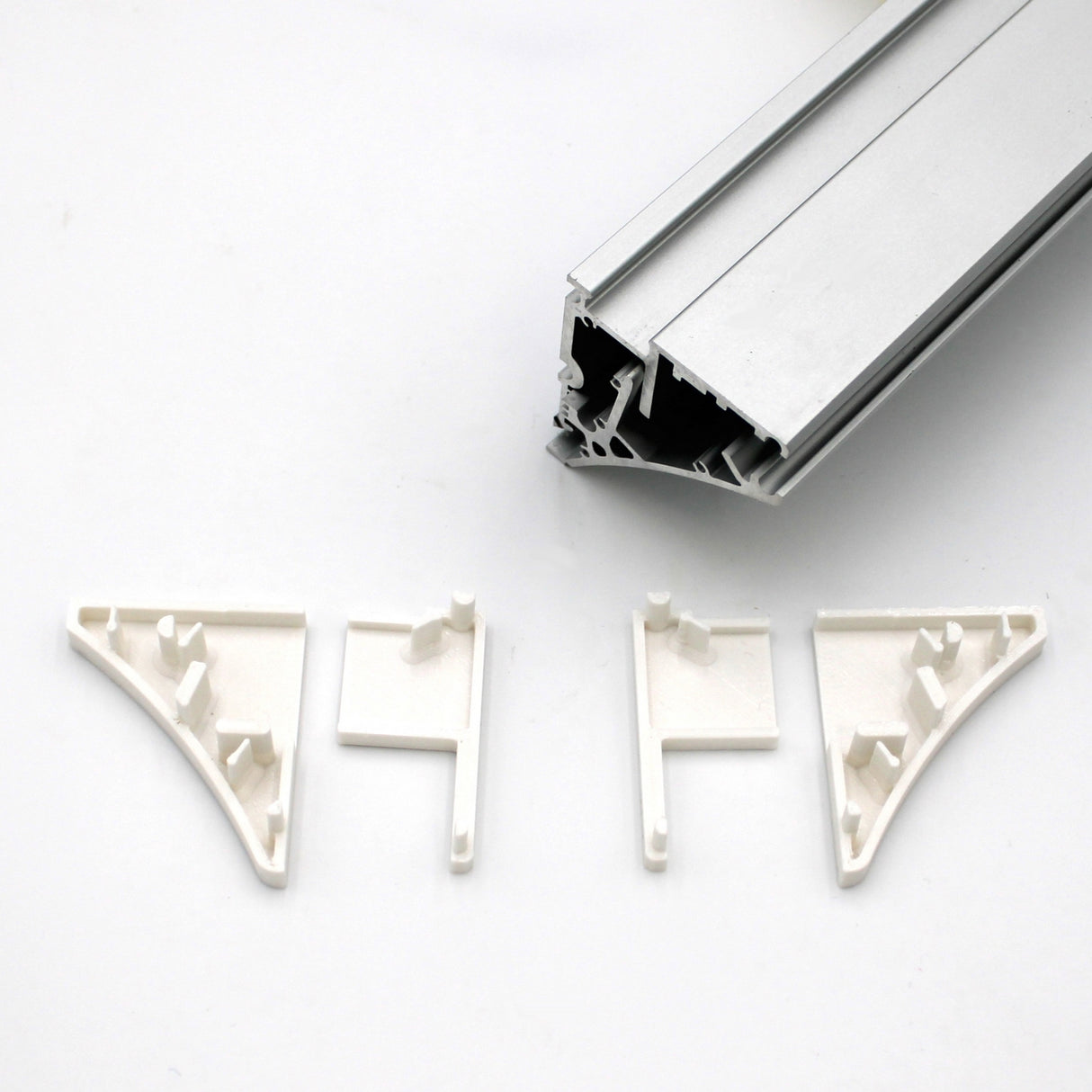 Four white End Caps for Pula P10 Profile are arranged below a Pula P10 edge-lit shelf profile rail with grooves, all displayed on a plain white background. The end caps are designed to fit and support the rail’s corners.