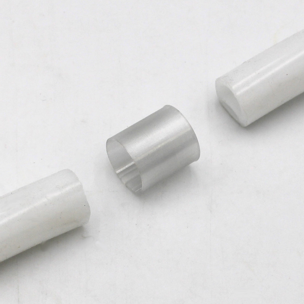 A Translucent Straight Joiner for Neon Redondo XL Profile is placed between two white cylindrical rods, resembling the Redondo XL profile, on a plain white background.