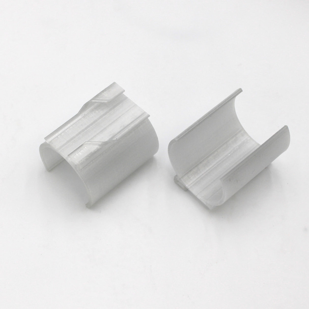 Two white Drop Ceiling T-Bar Clips for 1.5 round profiles, 3D printed with curved shapes, lie side by side on a white surface with their open sides facing outward—perfect for ceiling t-bar mounting.