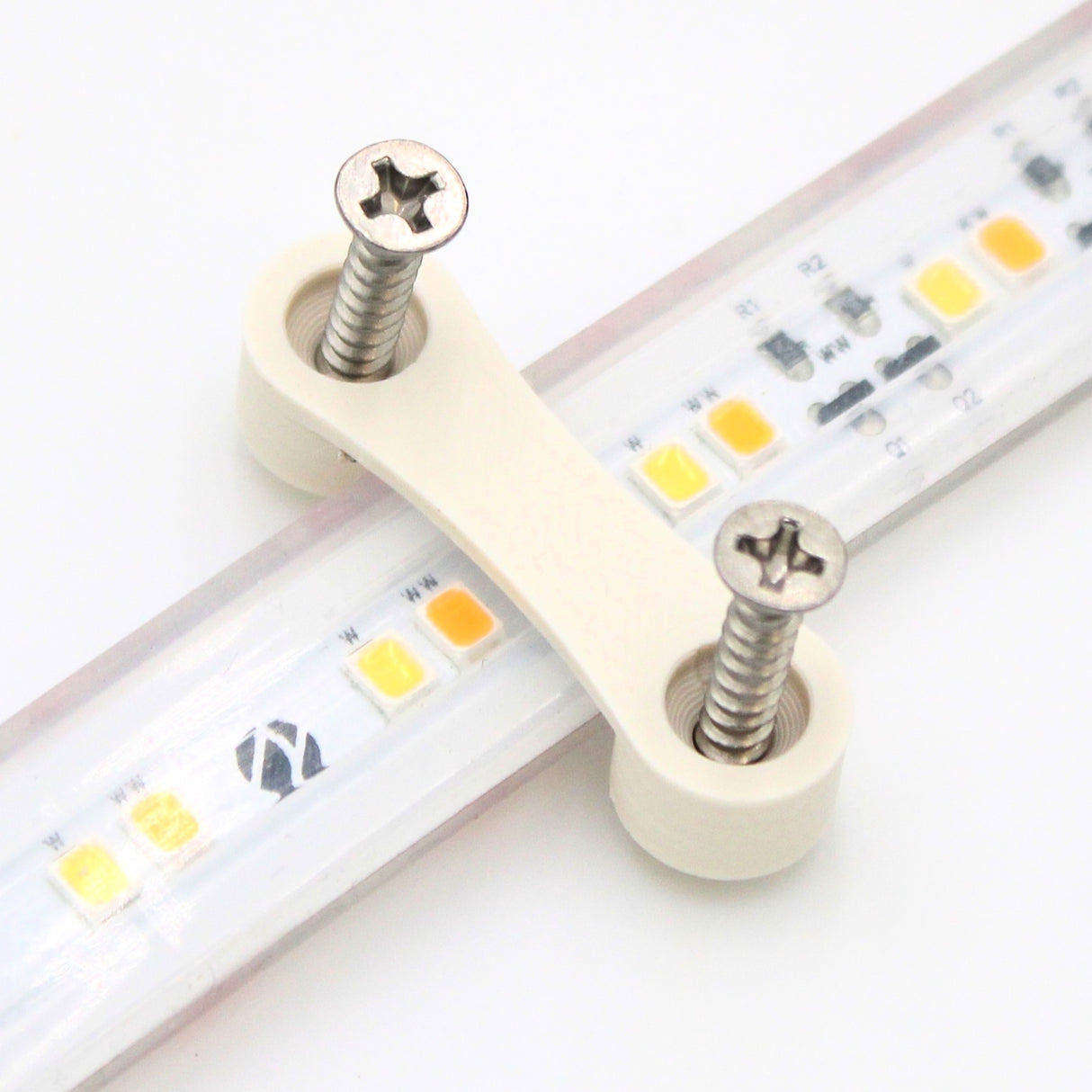 A close-up of the LED Strip Saddle, a white plastic bracket with two metal screws securing waterproof LED strips, shown against a white background to highlight its practical surface mount design.