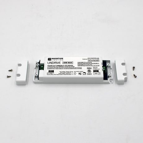 A Compact Electronic Phase Dimmable LED Driver (24V) ~ Magnitude LinDrive, white plastic housing open to show wiring terminals, sits on a white surface with four screws—perfect for under cabinet lighting.