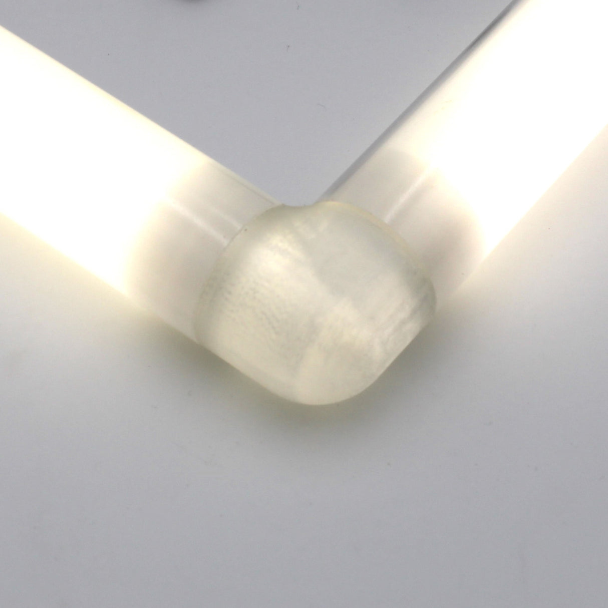 A close-up of two illuminated diffuser tubes connected at a right angle by a Translucent Elbow for Smokies38 Profile, set against a plain white background.