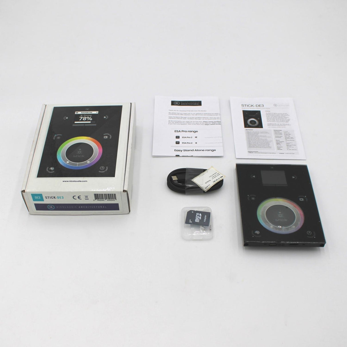 The Nicolaudie STICK-DE3 wall-mounted touch-sensitive DMX lighting controller kit includes the controller with color wheel, DMX box, manuals, USB cable, wall adapter, and microSD card—displayed on a white surface.