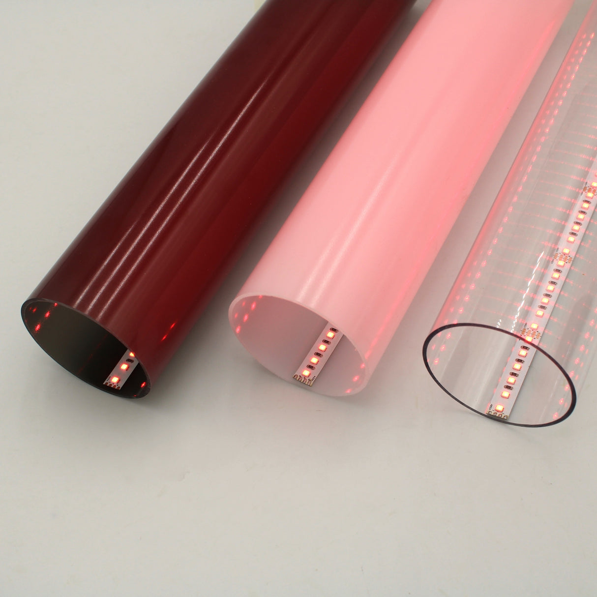 Three 2.75 Round Polycarbonate LED Lighting Tubes (Model Smokies70), each with an RGB Pixel LED Strip inside—one red, one pink, and one clear—are arranged side by side on a light gray surface.