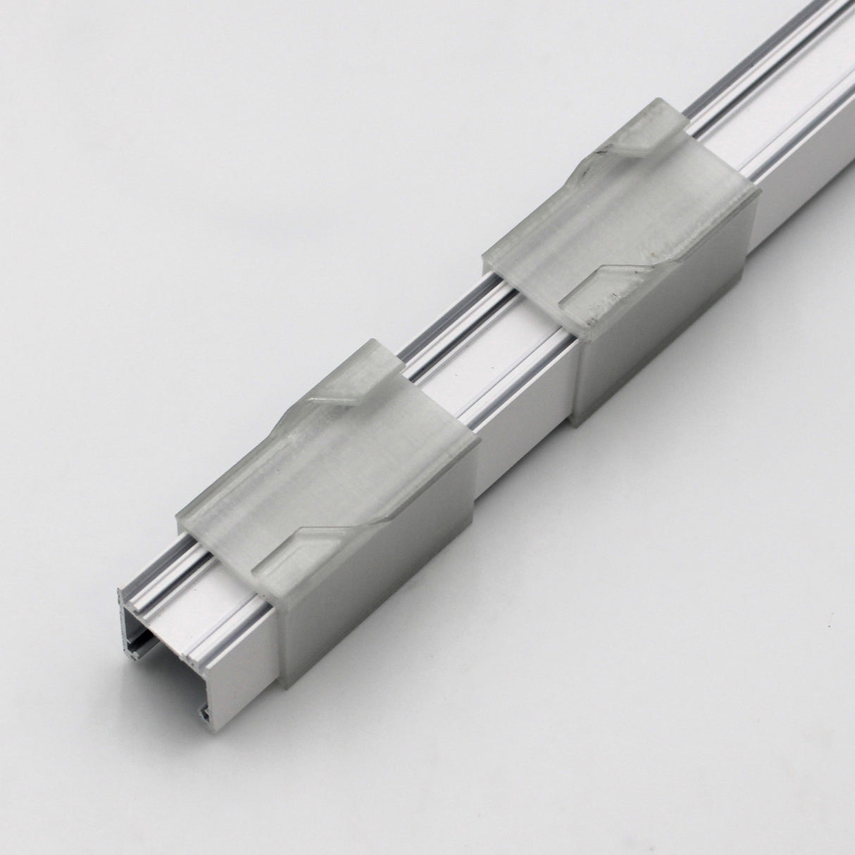 A Drop Ceiling T-Bar Linea20 Clip with two translucent gray brackets is mounted diagonally on a plain white background, demonstrating a drop-ceiling mounting solution.