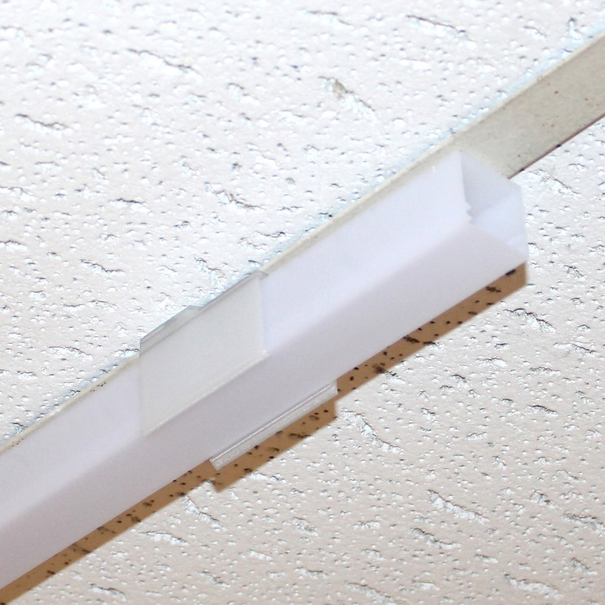 A close-up of a fluorescent ceiling light on a white speckled drop-ceiling, secured with a Visby Drop Ceiling T-Bar Clip.