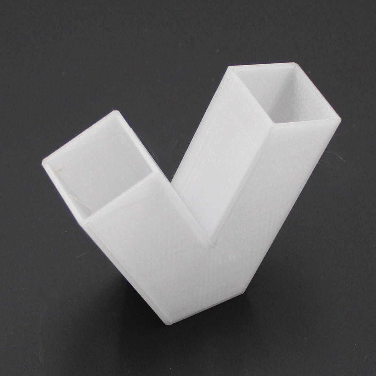 A translucent, 3D-printed Translucent Elbow for Visby Profile with rectangular hollow ends and a V-shaped design is placed on a dark surface.
