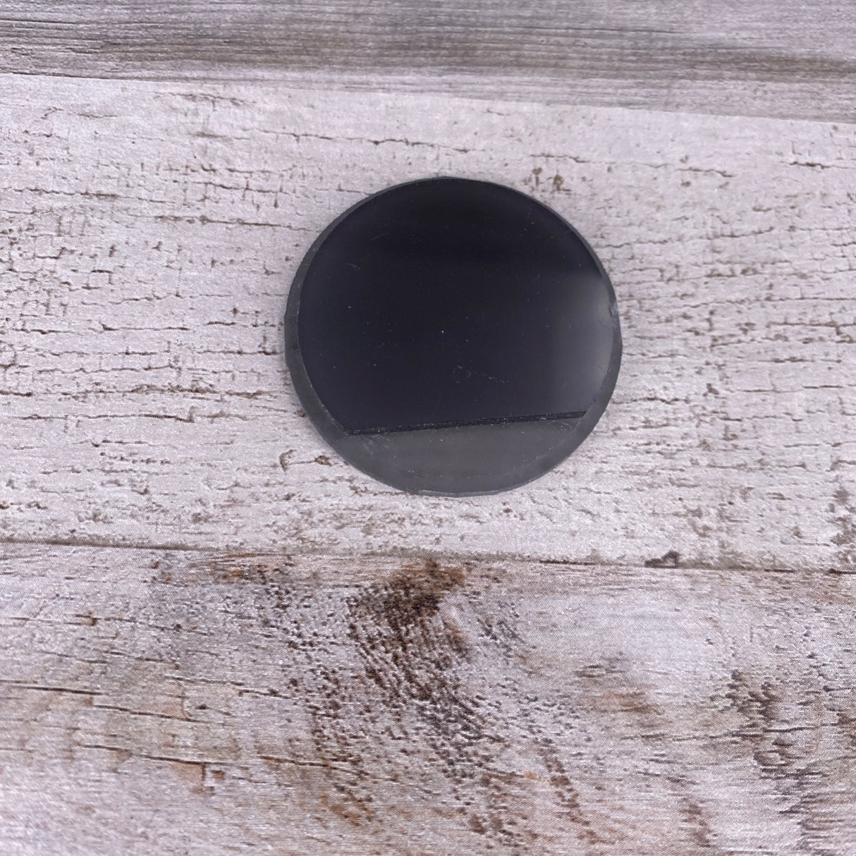 A black, round Plastic End Cap for Smokies38 Profile rests on a weathered, light gray wooden surface with a rustic texture.