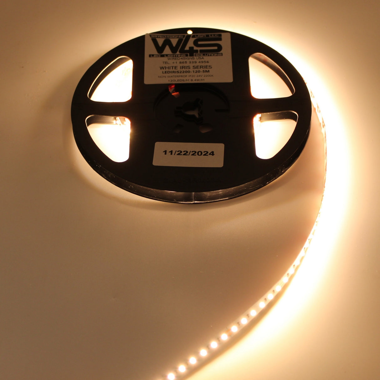 A partially unrolled White High CRI IP20 LED Strip (24V) ~ White Iris Series glows warm white on a light surface, with a label showing 11/22/2024 on the black reel. The strip delivers excellent color rendering.