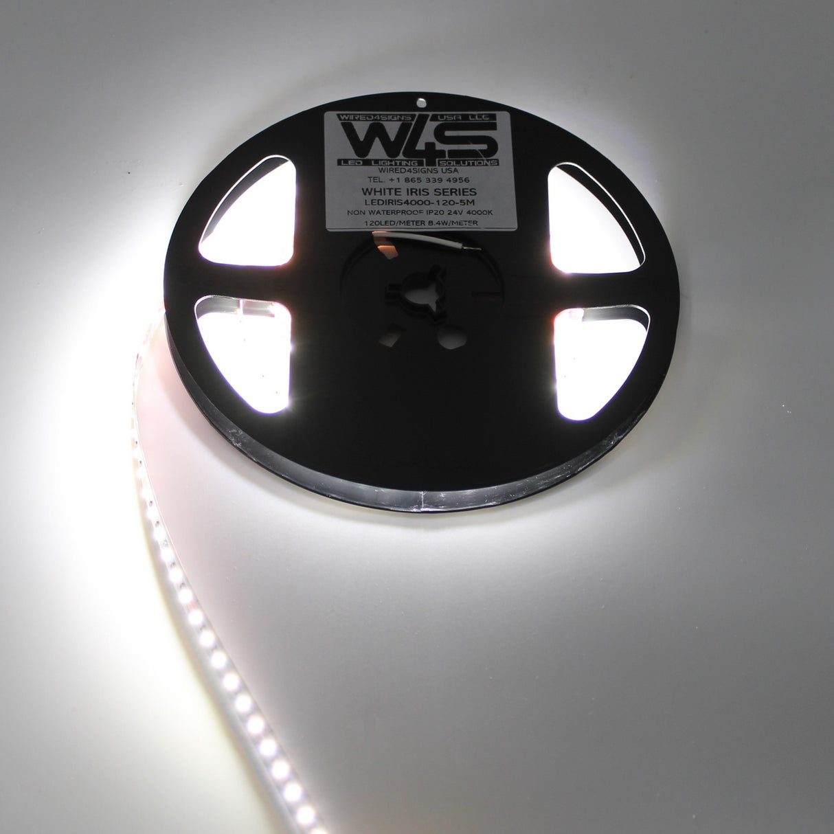 A spool of White High CRI IP20 LED Strip (24V) from the White Iris Series is partially unrolled and lit, casting a bright glow on a white surface.