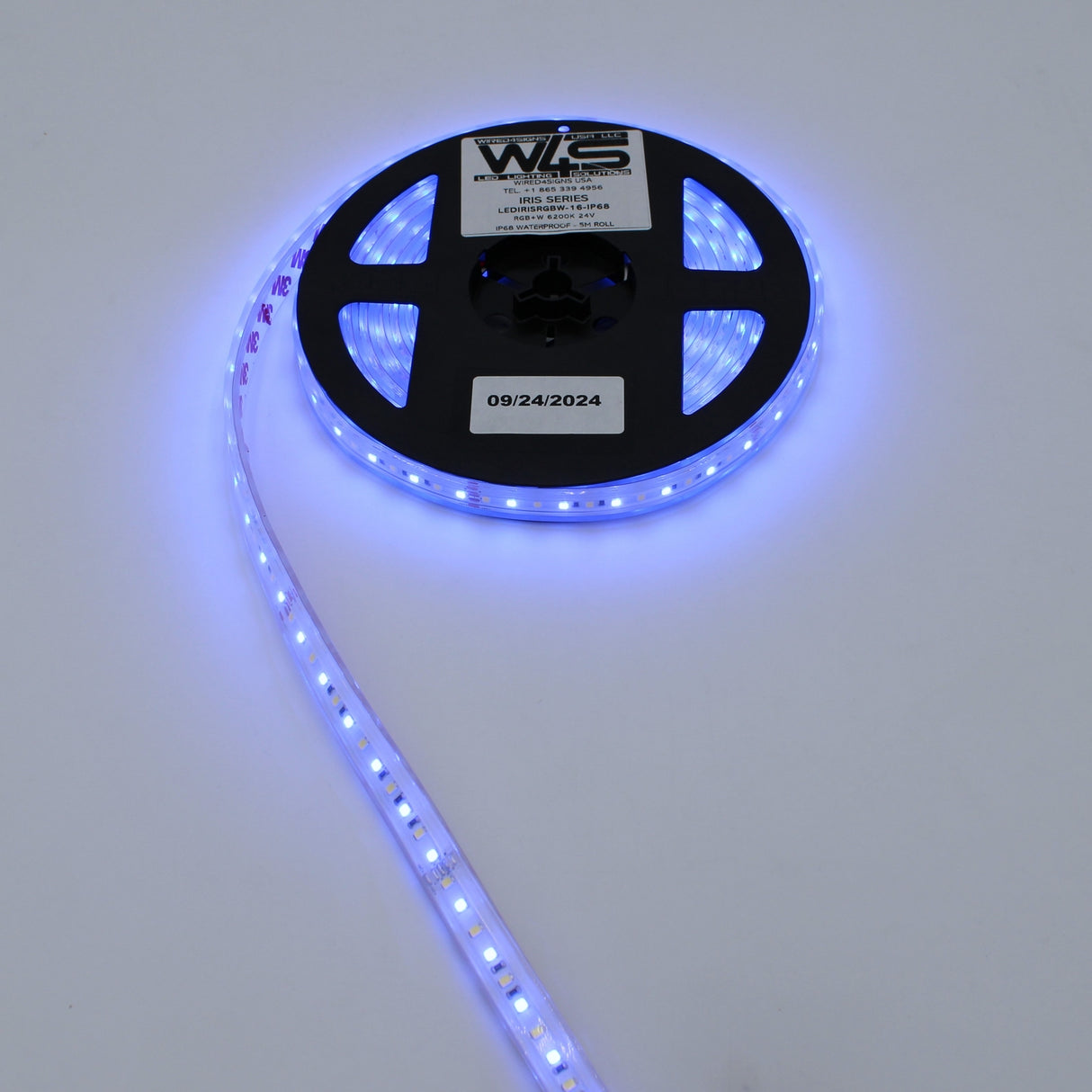 A spool of the High CRI RGBW IP68 Waterproof LED Strip (24V) ~ Iris Series is partially unrolled, glowing blue against a white background. The reel highlights its IP68 rating and 24V power for reliable, vivid illumination.