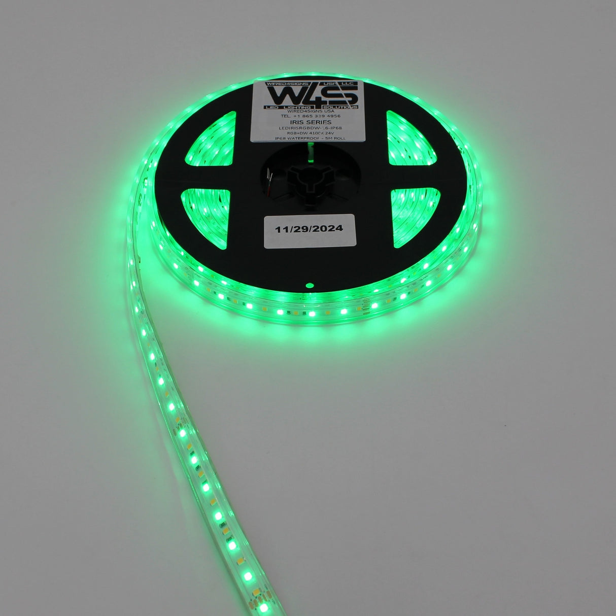 A reel of High CRI RGBW IP68 Waterproof LED Strip (24V) ~ Iris Series is partially unrolled and glowing brightly on a white surface, with a white label showing text and the date 11/29/2024 at the reel’s center.