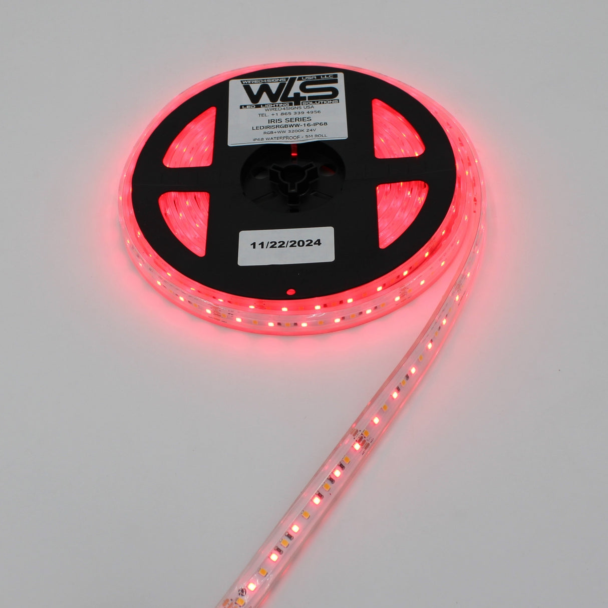 A roll of High CRI RGBW IP68 Waterproof LED Strip (24V) ~ Iris Series glows pink, partially unspooled with a WLS label and 11/22/2024 on the black reel, displayed against a plain white background.