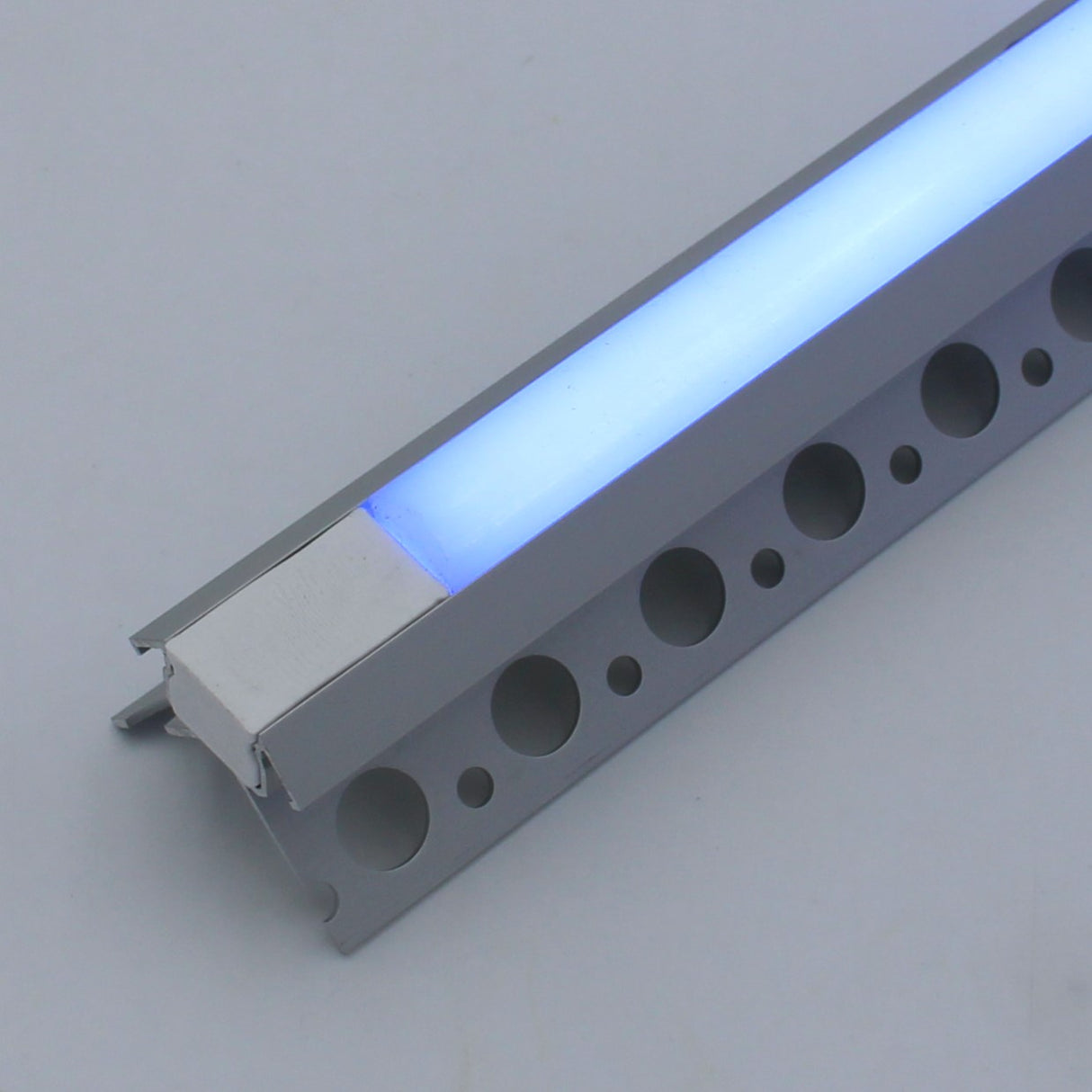 A close-up of the RGB LED Tile Light Strip Kit for Outside Corners (24V) ~ Nicho Series, featuring a glowing blue cover and mounted in an aluminum channel with circular cut-out holes along the edge.