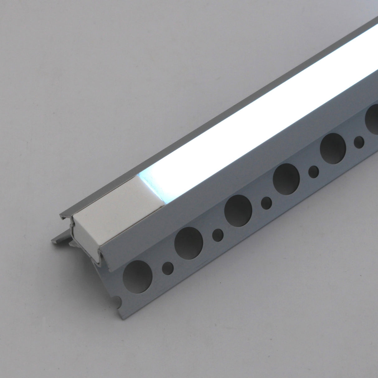 A close-up of the RGB LED Tile Light Strip Kit for Outside Corners (24V) ~ Nicho Series, a slim rectangular waterproof light in a silver aluminum channel with circular side holes, resting on a plain surface.