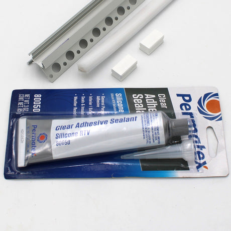 A White LED Tile Light Strip Kit for Outside Corners (24V) ~ Nicho Series in its packaging rests on a white surface beside a metal bracket, plastic rods, two white rectangular blocks, and an aluminum LED channel.