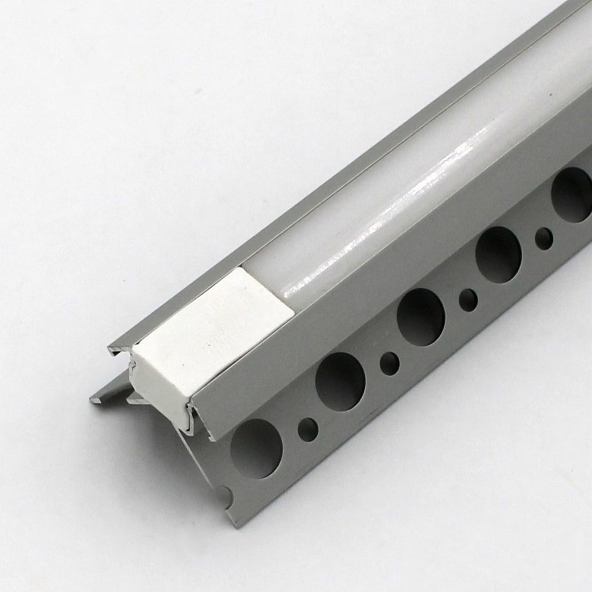 A close-up of the Nicho Series White LED Tile Light Strip Kit for Outside Corners (24V), featuring an aluminum channel with round perforations and a white plastic insert, displayed at an angle to highlight its profile and mounting edge.