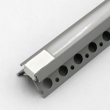 A close-up of the Nicho Series White LED Tile Light Strip Kit for Outside Corners (24V), featuring an aluminum channel with round perforations and a white plastic insert, displayed at an angle to highlight its profile and mounting edge.