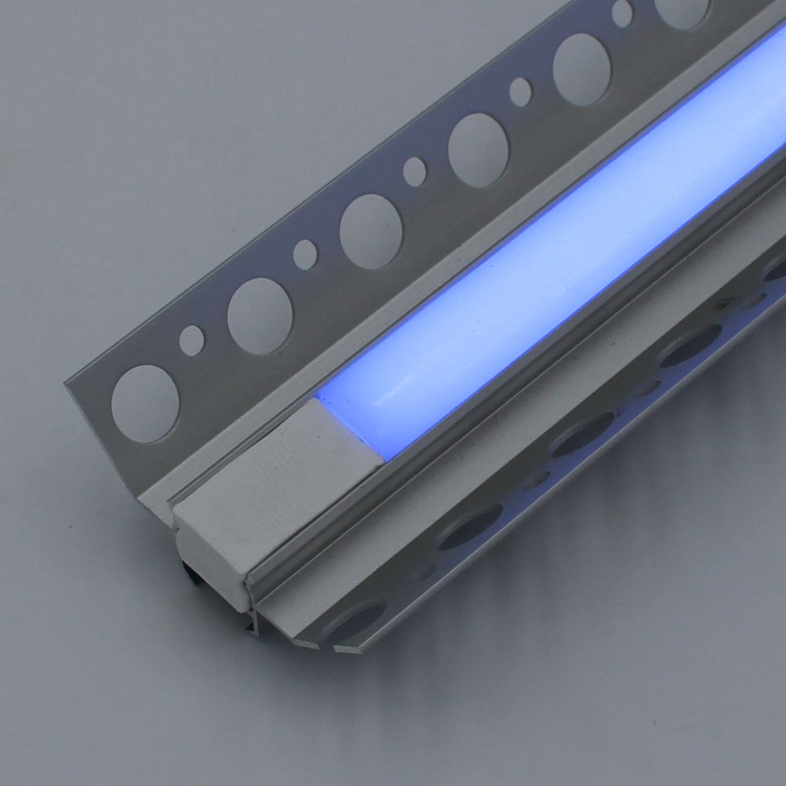 A close-up of the Nicho Series RGB LED Tile Light Strip Kit for Inside Corners (24V), featuring circular cutouts in a modern aluminum channel, emits a soft blue glow against a plain gray background.