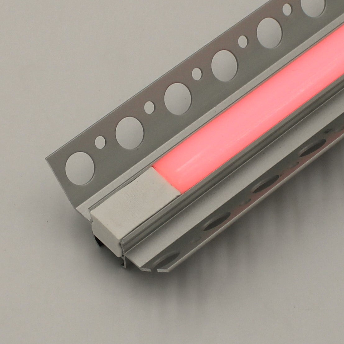 A close-up of the RGB LED Tile Light Strip Kit for Inside Corners (24V) ~ Nicho Series, an aluminum channel with circular cutouts and a glowing pink strip, set against a light gray background.