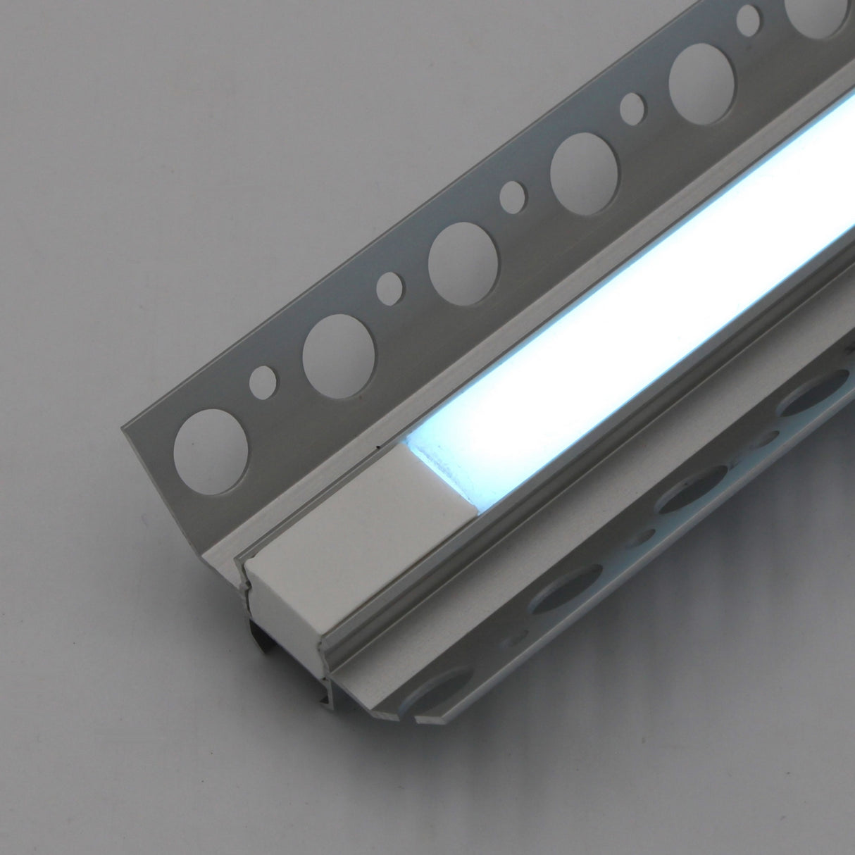 Close-up of the RGB LED Tile Light Strip Kit for Inside Corners (24V) ~ Nicho Series, installed in a slim aluminum channel with circular cutouts, casting a cool white glow on a light gray background.