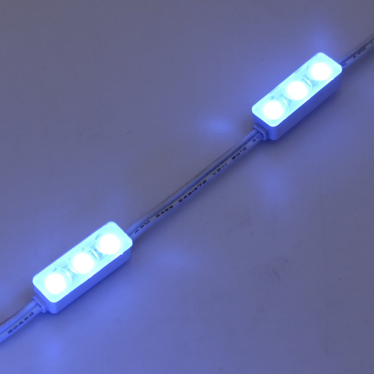 Two Mini3 Color 160 Mini LED Modules from the Wide Angle Series, each with three bright white-blue LEDs, are linked by a white cable and glow vividly against a plain white background.
