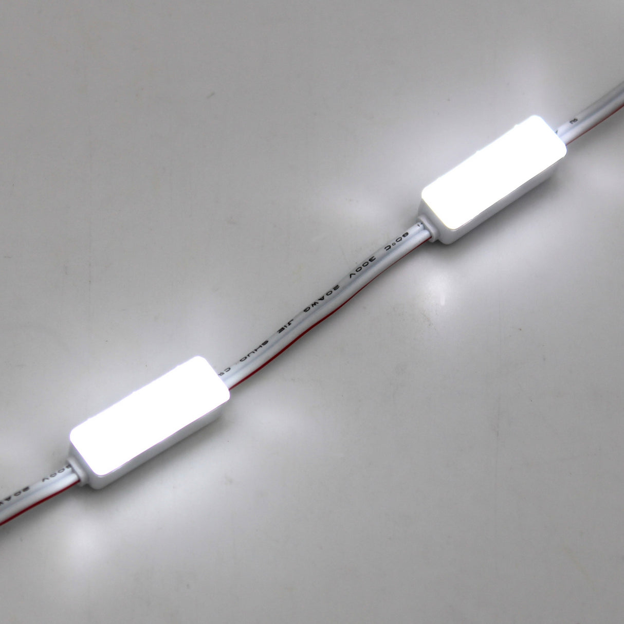 Close-up of the Mini3 White 160 Mini LED Module from the Wide Angle Series, featuring rectangular white modules with wide-angle lenses, glowing brightly and connected by wires on a white surface.