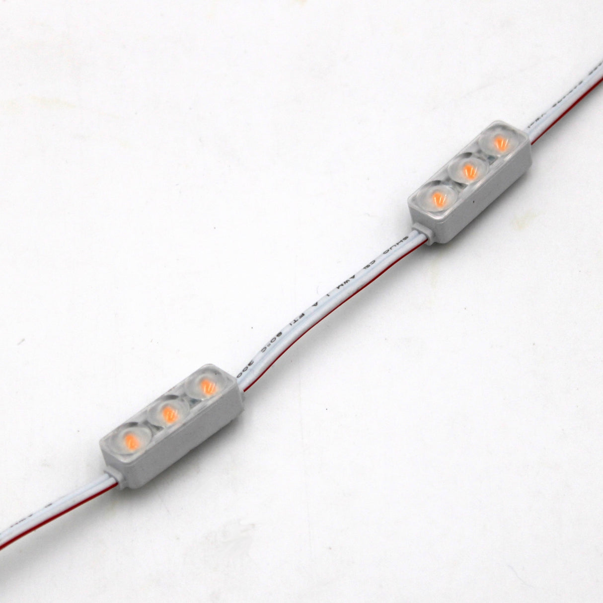 Close-up of two Mini3 Color 160 Mini LED Module ~ Wide Angle Series, each rectangular, waterproof IP68 with four glowing LEDs, attached to a white wire with red and black lines on a plain white surface.