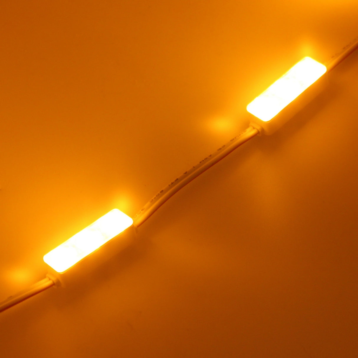 Two Mini3 Color 160 Mini LED Modules from the Wide Angle Series, in warm yellow, are connected by a white wire and glow brightly against a yellow background.