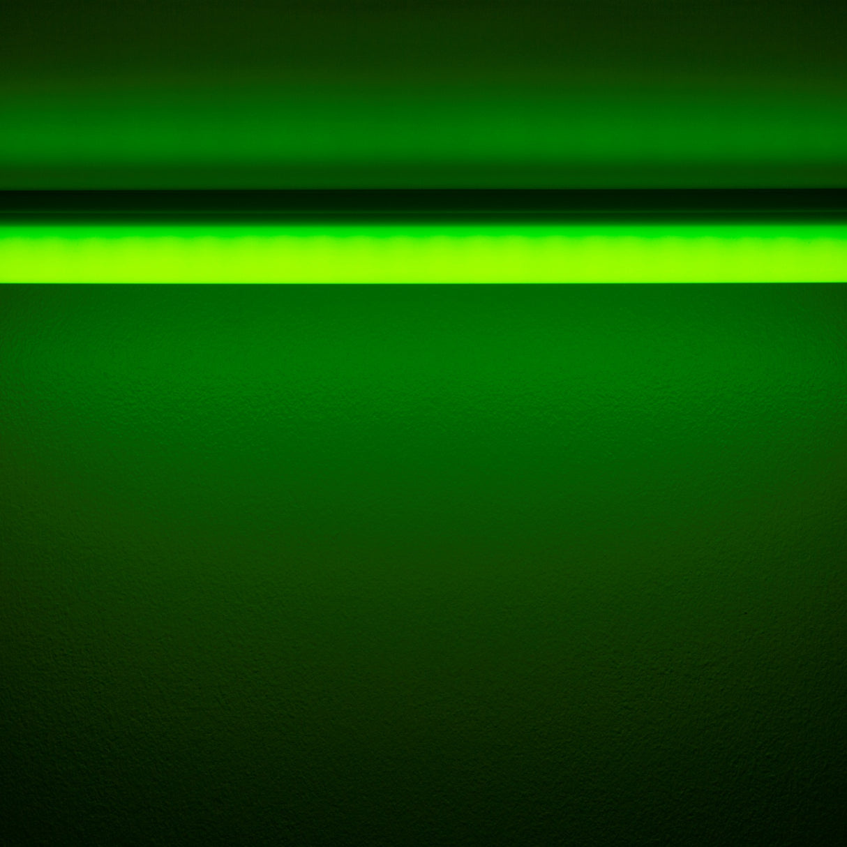 The Colored Border Contour Tube Light ~ Hi-Lite 30 Straight Section casts green light onto a dark wall from above, creating a vivid glowing gradient of green across the surface.