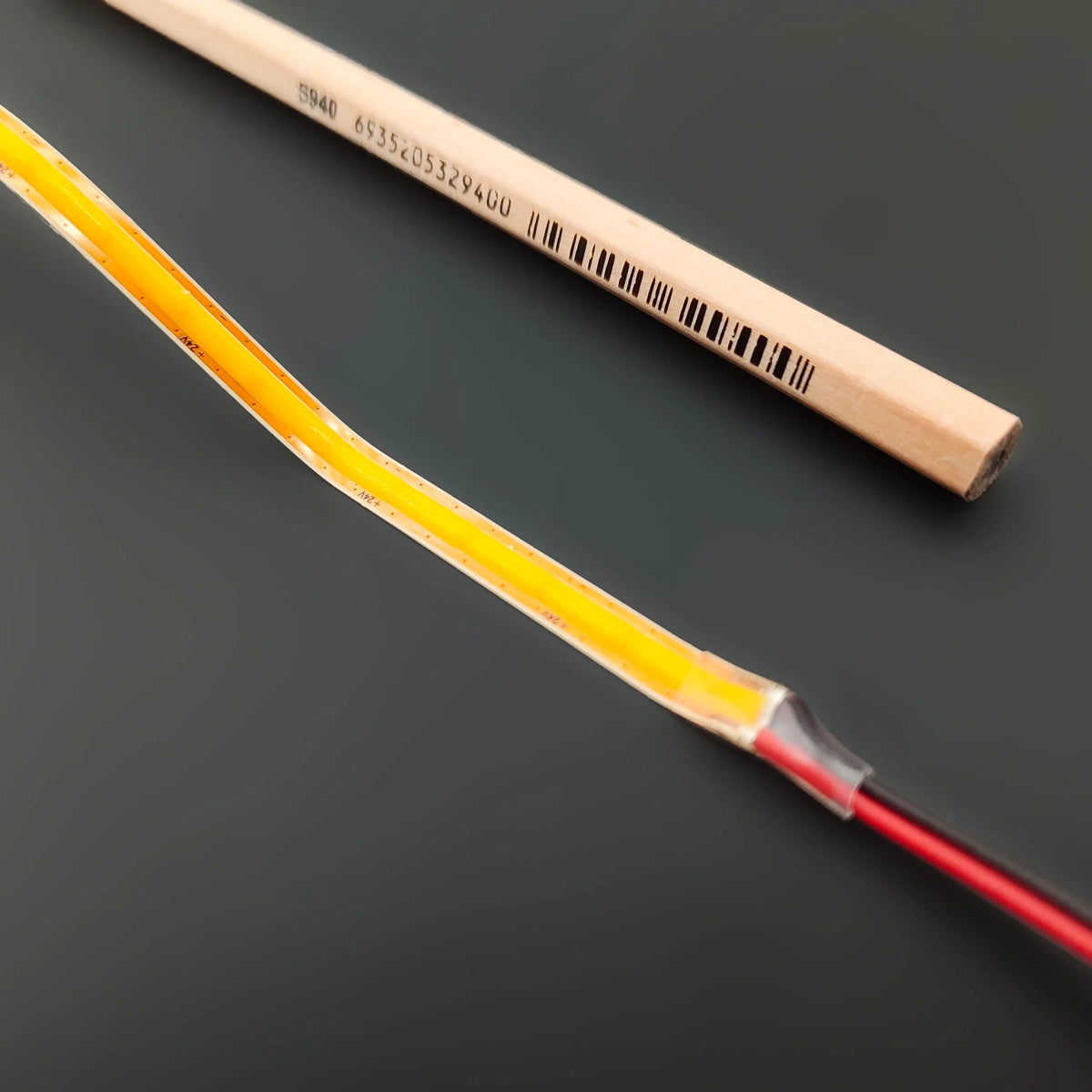 An ultra-thin, flexible yellow Ultra-Thin Flexible COB IP20 High CRI LED Strip (24V) ~ EnoLed Micro Series next to a wooden pencil with a barcode.
