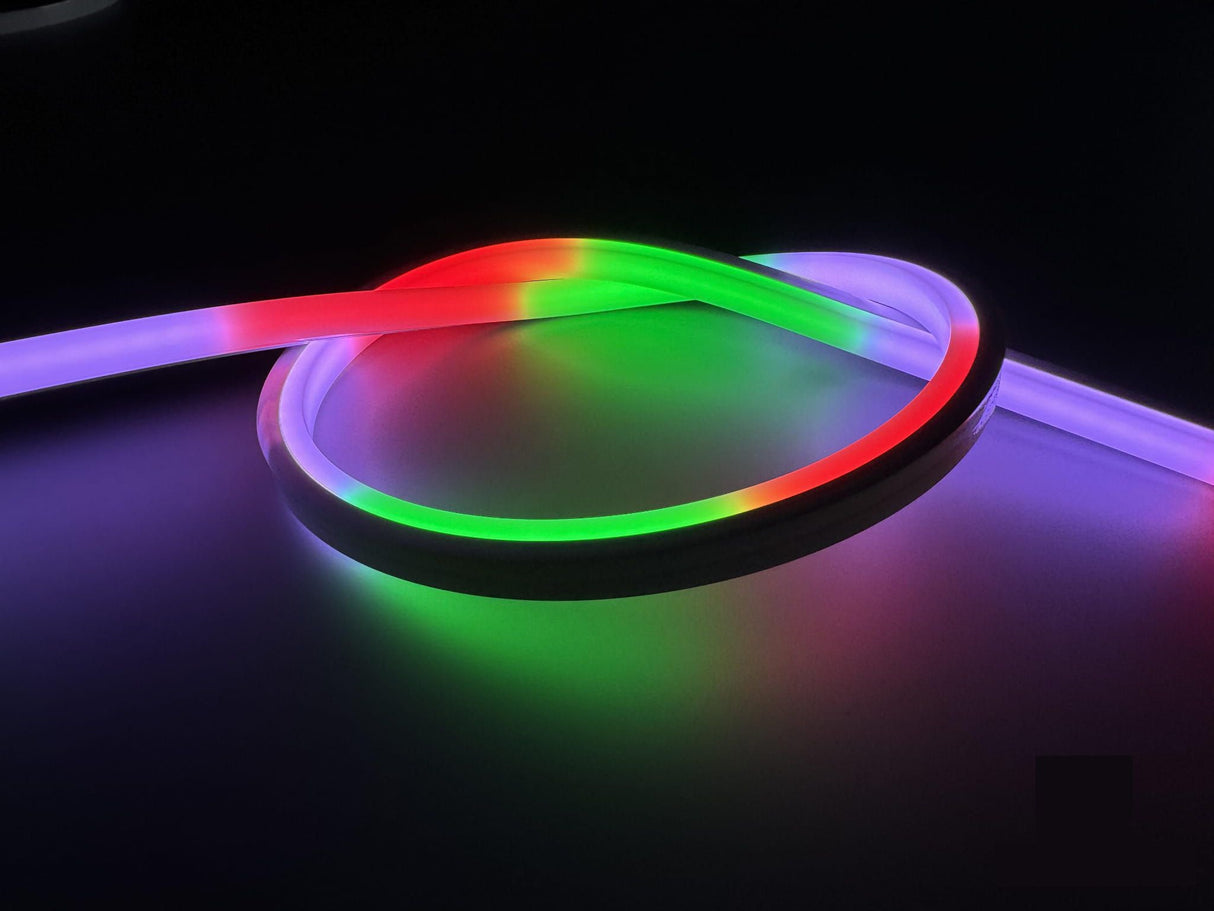 The Pixel IP44/IP66 Neon Flexible LED Light Line (24V) ~ Flex Slim Series glows in red, green, and purple, forming a loose loop on a dark surface.