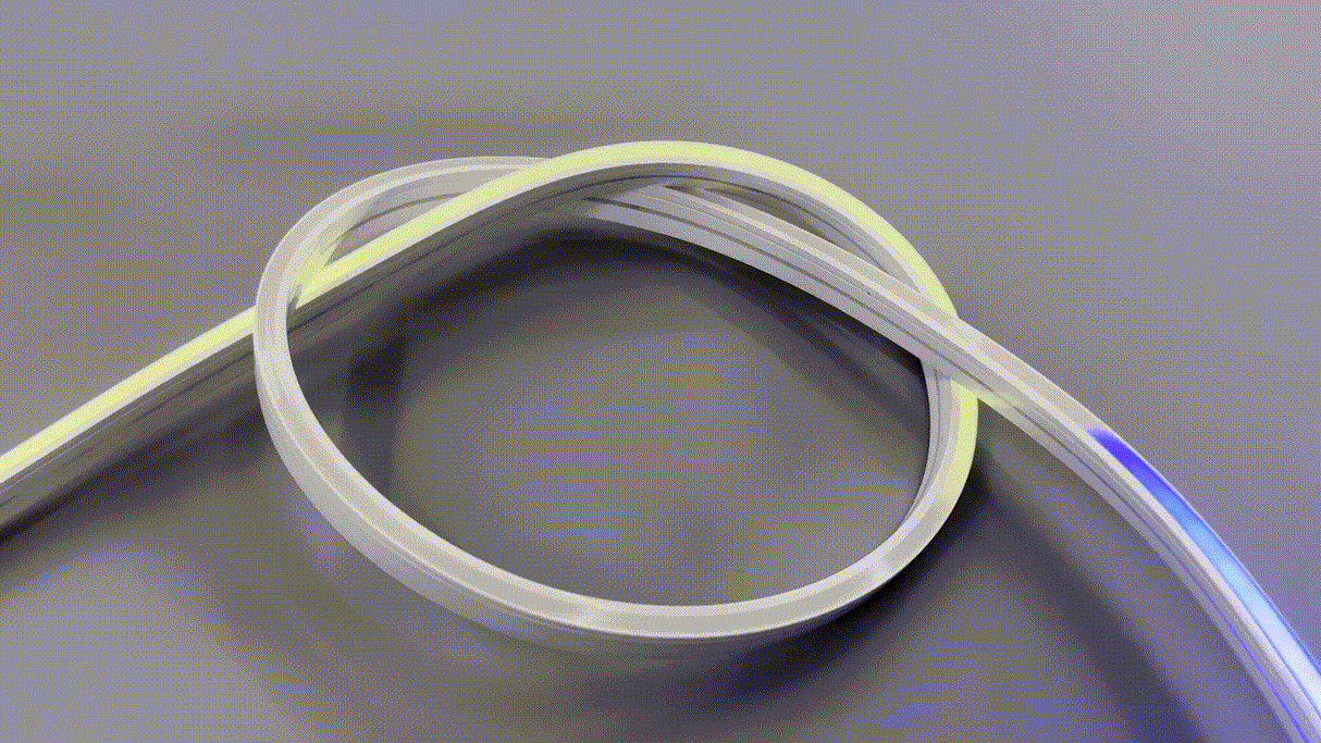 The Pixel IP44/IP66 Neon Flexible LED Light Line (24V) ~ Neon Flex Super Slim Pixel Series, shown looped on a gray surface, emits a glowing yellow edge with a hint of blue at the end—perfect for striking architectural lighting accents.