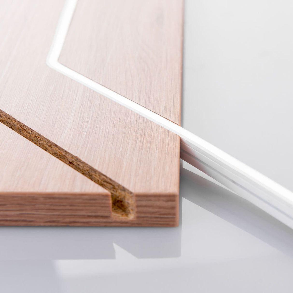 Close-up of a wooden panel with a precision-cut groove next to a Pixel IP44/IP66 Neon Flexible LED Light Line (24V) ~ Neon Flex Super Slim Pixel Series, fitting perfectly for sleek architectural lighting on a glossy white surface.