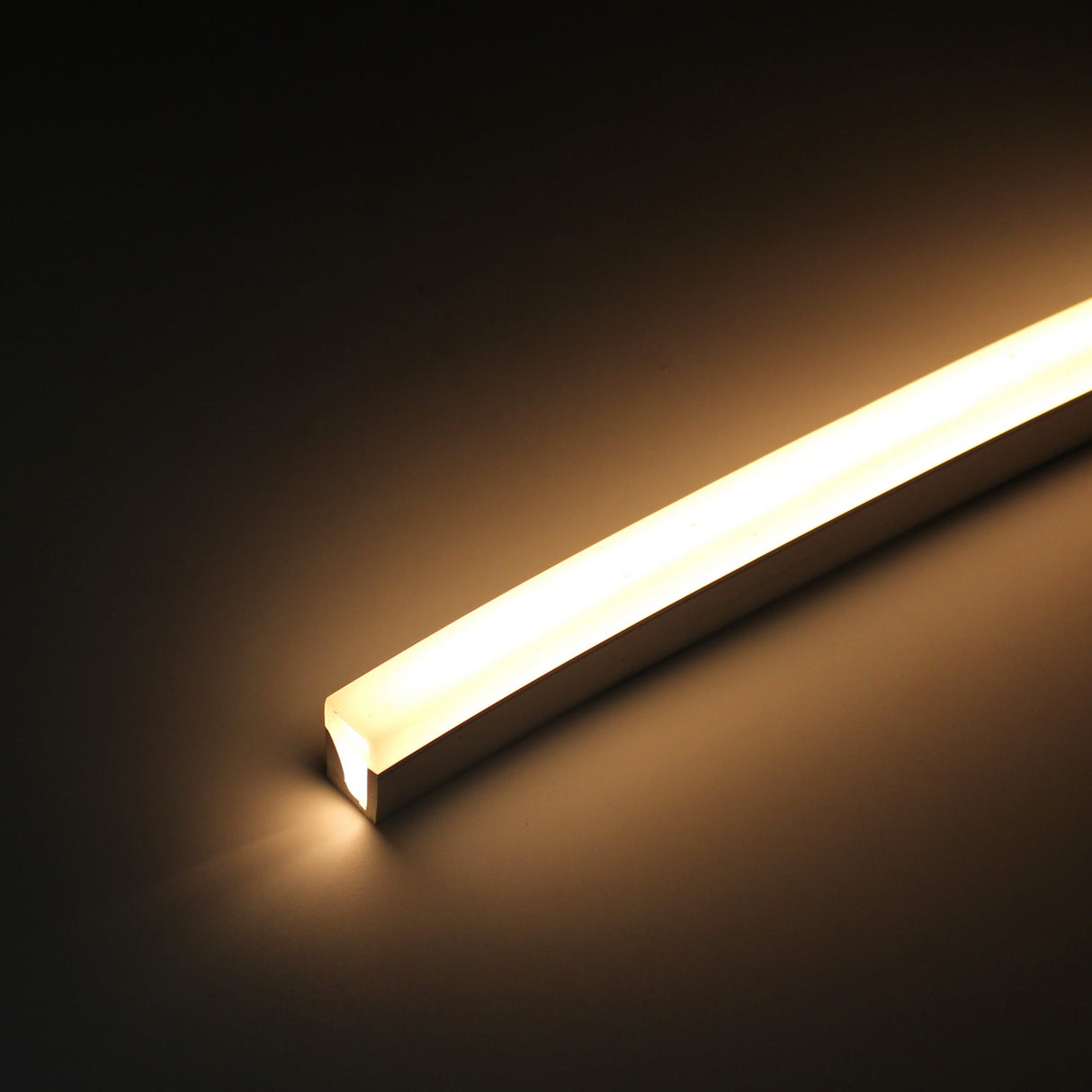 The Flexible LED Neon Light Silicone Profile ~ Model Neon Las Vegas emits a warm yellow glow, illuminating its surroundings. The flexible strip is shown diagonally against a dark background, ideal for decorative lighting.