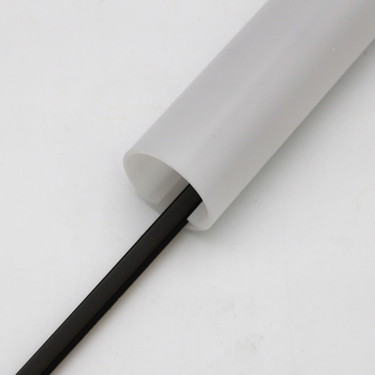 A Black IP65 Neon LED Light Line (24V) from the Optimum Black Neon Max Series is partially inserted in a white cylindrical conduit, set against a plain white background.
