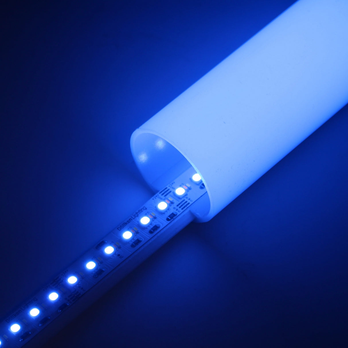 The RGB+CCT IP20 LED Strip (24V) ~ Optimum Cromatic Series glows brightly in a white cylindrical tube, displaying vibrant colors and tunable white lighting against a dark background.