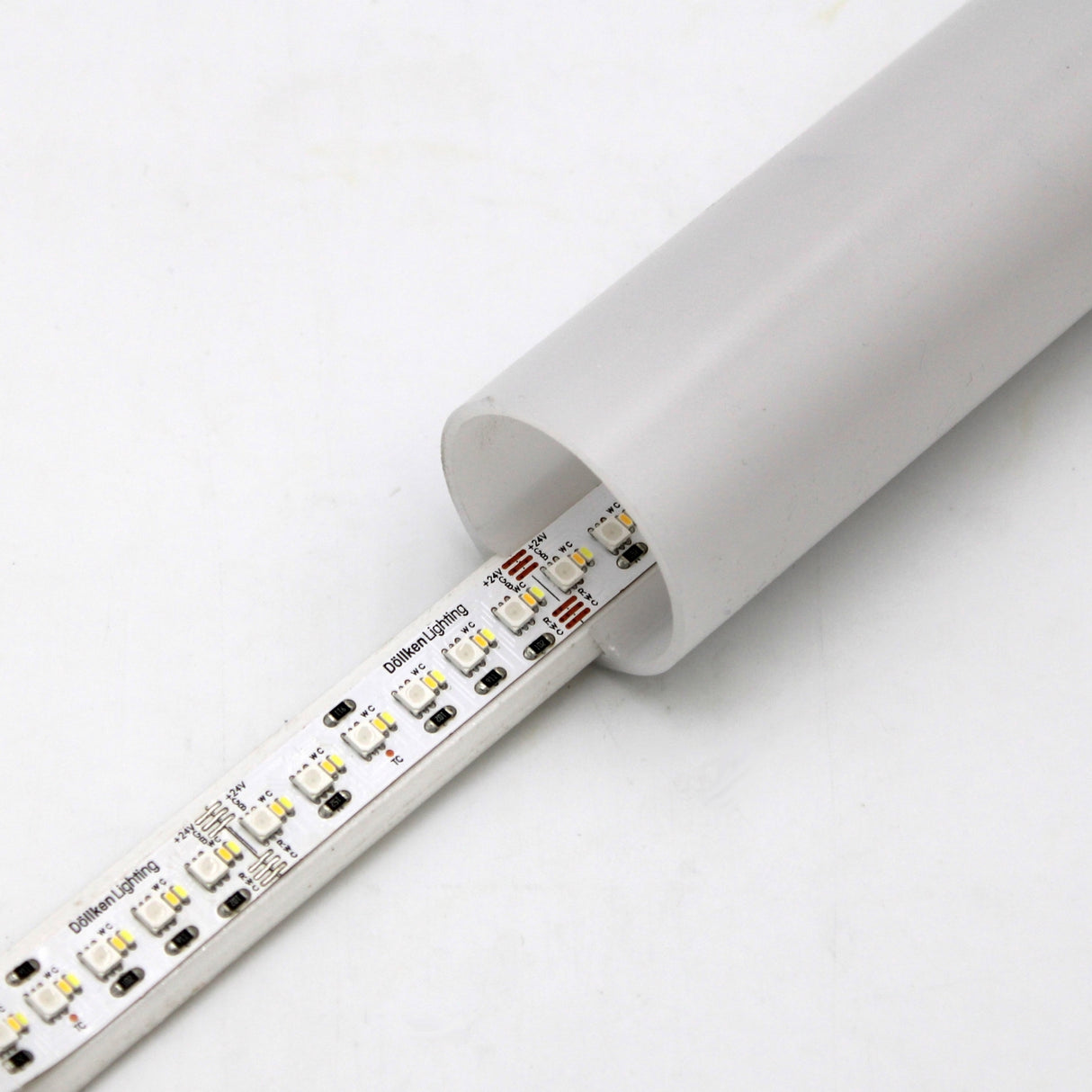 A close-up of the energy-efficient RGB+CCT IP20 LED Strip (24V) from the Optimum Cromatic Series, partially inserted into a white cylindrical tube against a plain white background.