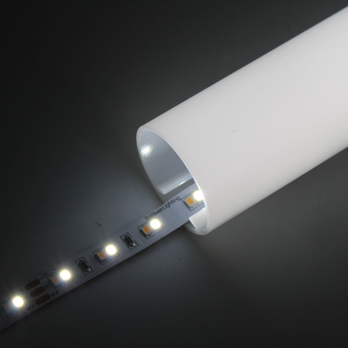 The High-CRI Tunable White IP20 LED Strip (24V) ~ Optimum Harmony Series is shown glowing as it’s inserted into a white cylindrical diffuser tube on a dark background, demonstrating its adjustable color temperature.