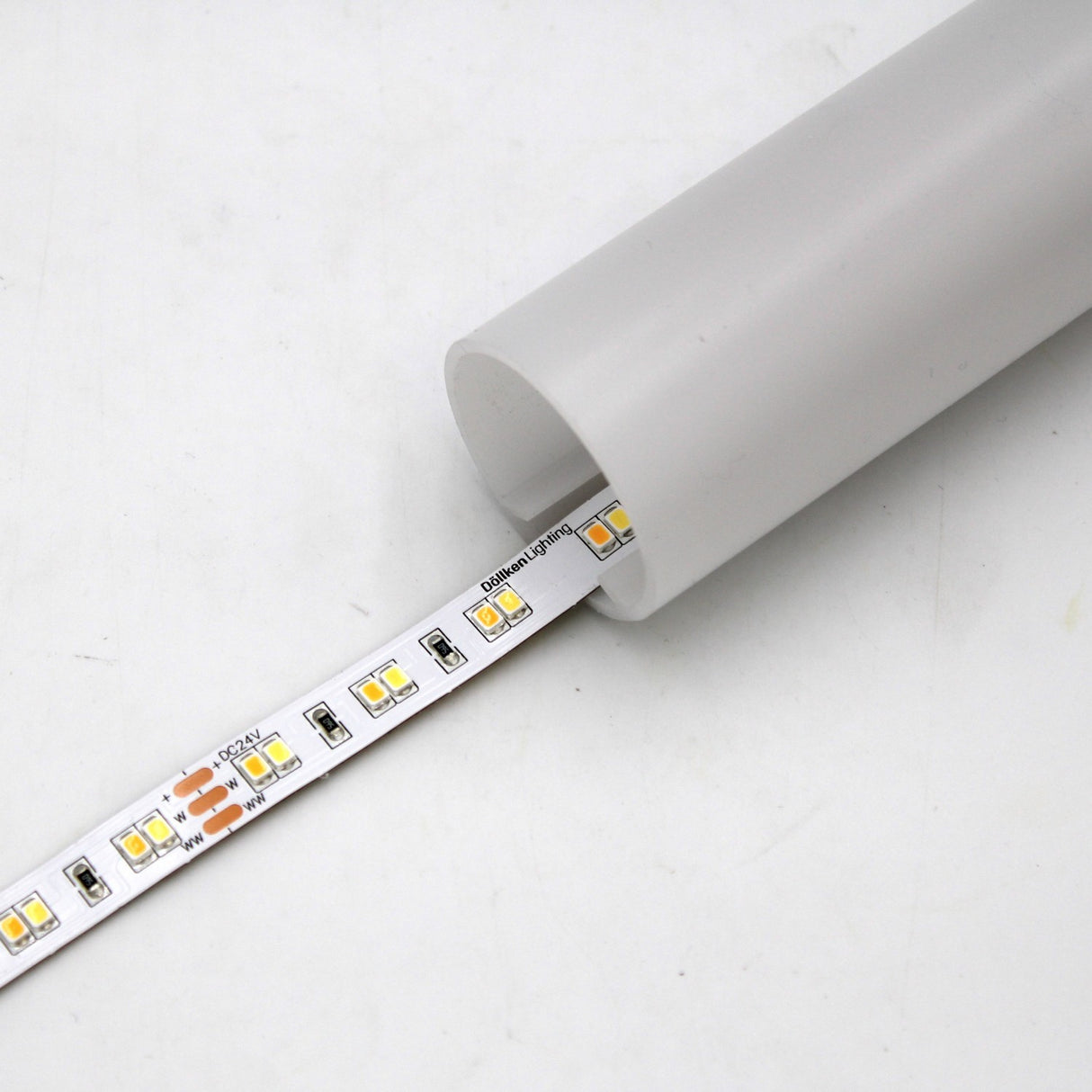 A High-CRI Tunable White IP20 LED Strip (24V) from the Optimum Harmony Series is partially inserted into a translucent, cylindrical plastic housing on a white surface.