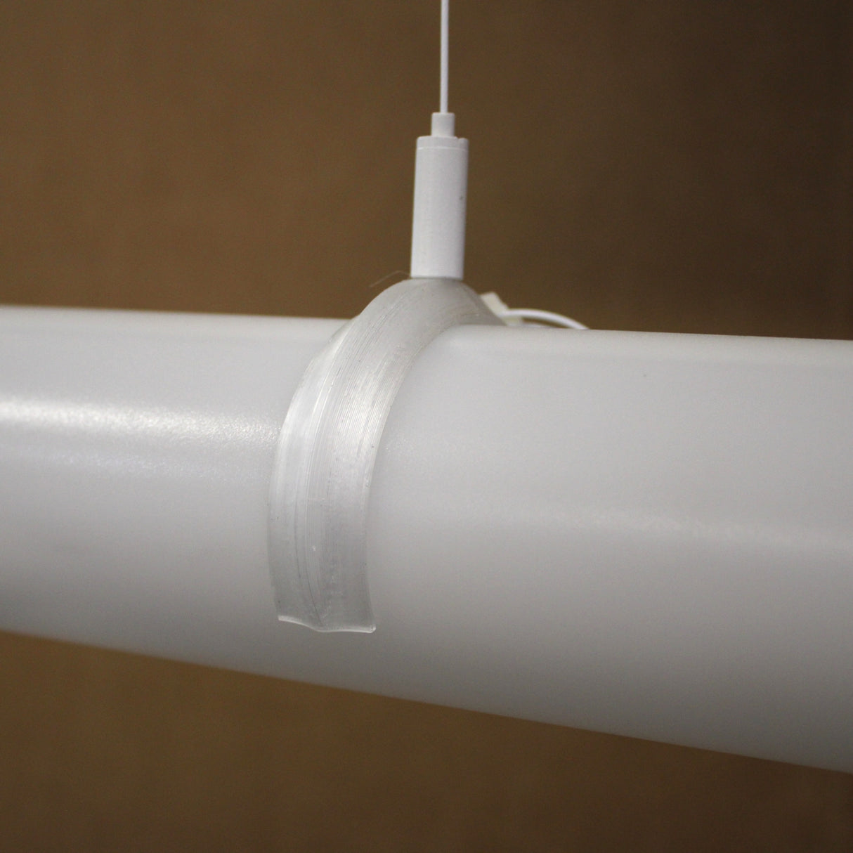 A translucent Mounting Clip for 2.56" Round Profiles secures a white cylindrical rod, with a thin white cord attached to the clip, all set against a plain brown background.