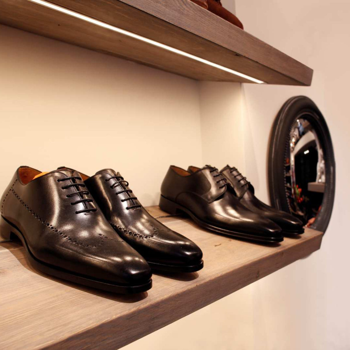 Two pairs of polished black dress shoes rest on a wooden shelf, subtly lit by the 0.39 Recessed LED Channel (Model Smart-In10) that creates a seamless line of light. A round mirror on the right reflects part of the sophisticated room.
