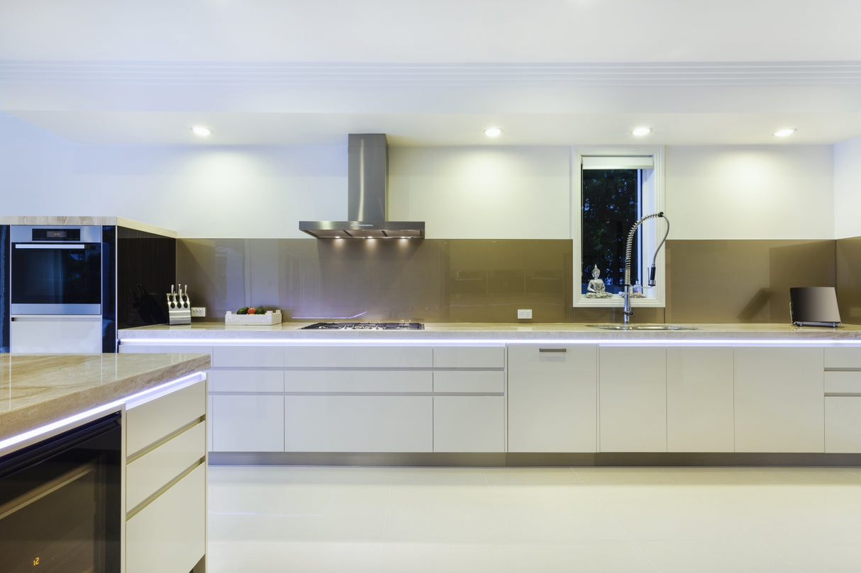Modern kitchen with glossy white cabinets, built-in oven, gas stove with range hood, integrated sink and tall faucet, knife block, and sleek lighting using the Smart10 Miniature Surface Mount LED Channel beneath cabinets, plus a small window above the sink.