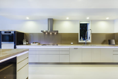 Modern kitchen with glossy white cabinets, built-in oven, gas stove with range hood, integrated sink and tall faucet, knife block, and sleek lighting using the Smart10 Miniature Surface Mount LED Channel beneath cabinets, plus a small window above the sink.