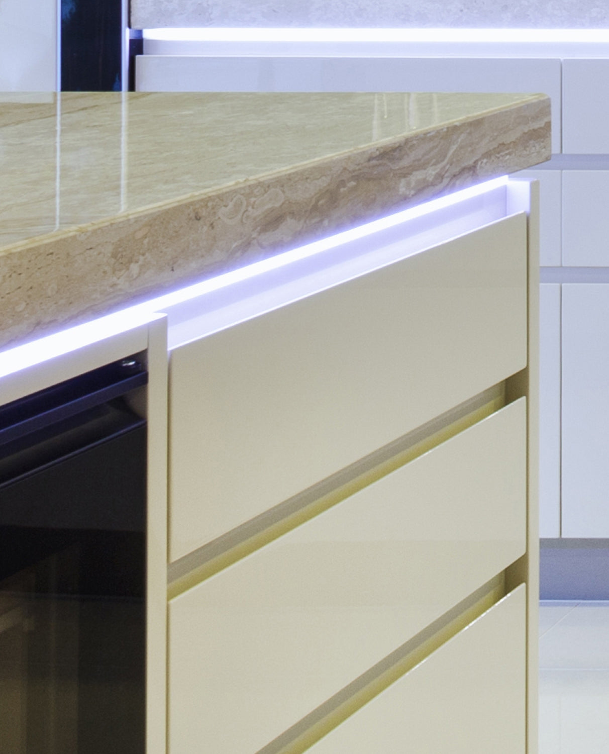 Close-up of a modern kitchen counter with a beige stone surface, cream drawers, and the Miniature Surface Mount LED Channel ~ Model Smart10 for integrated strip lighting under the countertop, creating a stylish contemporary look.